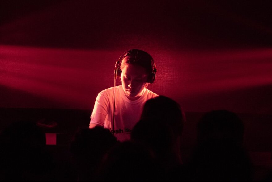 A DJ in a dimly lit setting, heavily saturated with dramatic red lighting.