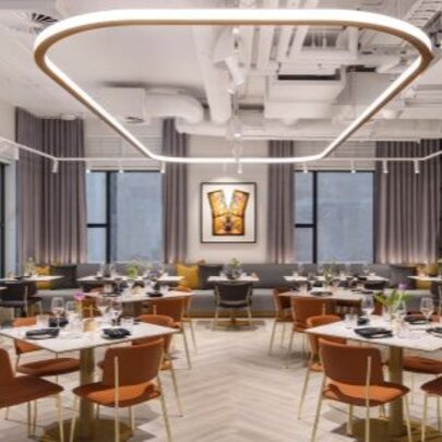 The modern interior of a restaurant with widely spaced square tables and bench seating along the back windows.