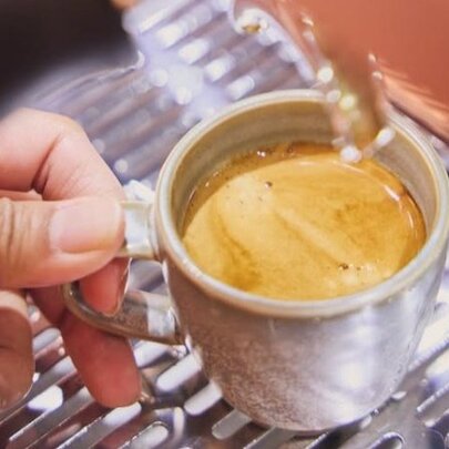 A freshly poured small espresso cup on the metal grate of a coffee machine.