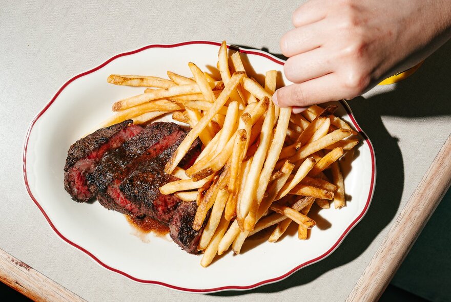 A white plate with a sliced steak and plenty of fries.