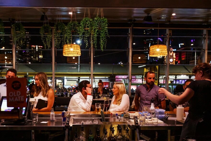 People seated at a long bar with staff, glasses, bottles and point of sale screen.