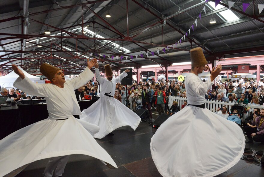 Traditional whirling dervish danceres in white costumes under a shed roof. 