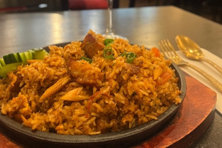 A Thai-style rice dish on a black table with cutlery.