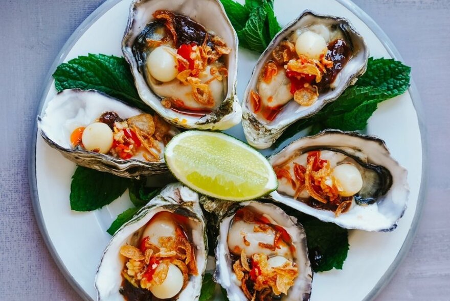 A plate of oysters with garnishes and a wedge of lime in the centre. 