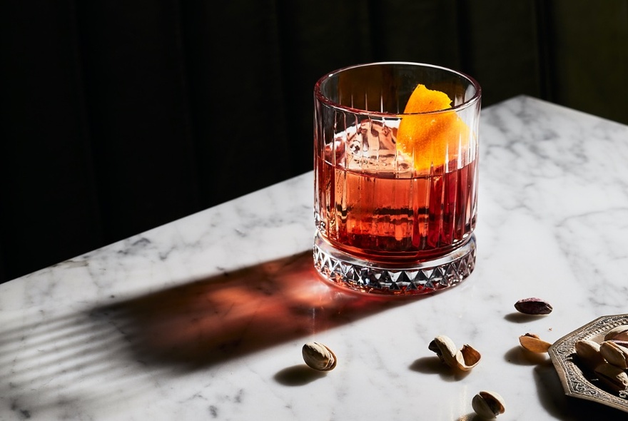 A drink in a tumbler with a slice of fruit.