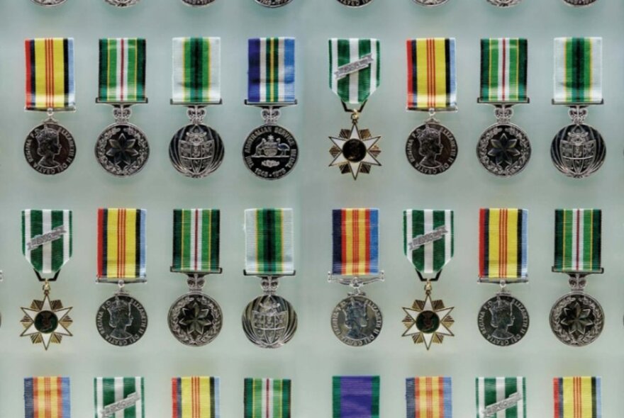 Australian military medals displayed with their ribbons in a glass case.