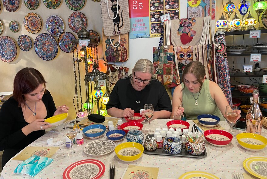 A craft workshop with three women at a table decorating bowls. 