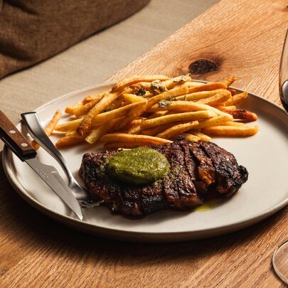 A white plate with steak and chips on a wooden table with glass of wine