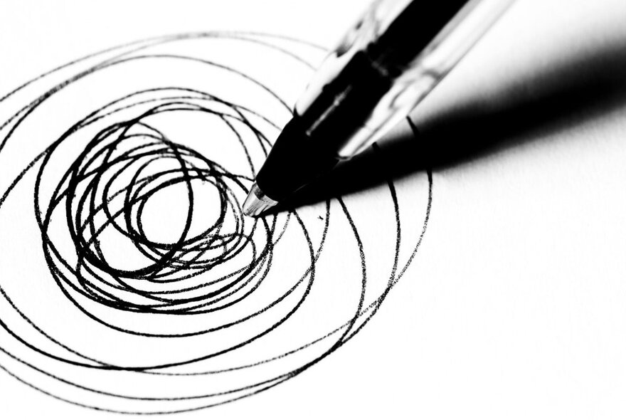 A black and white image of a pen drawing spirals on a page. 