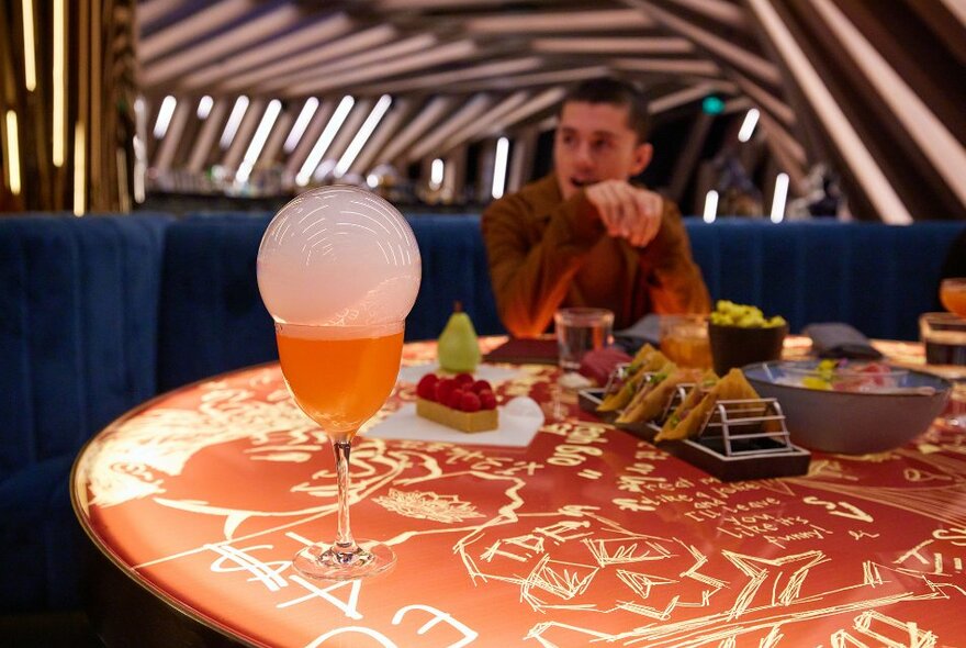 A fancy cocktail with a bubble on top and snacks in a cocktail bar.