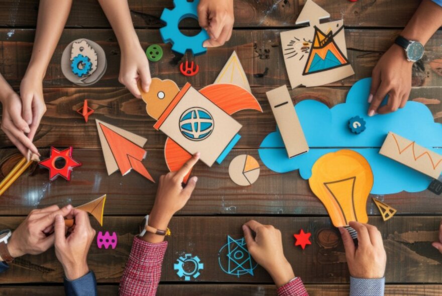 Looking down from above at a craft table with children's hands visible making model hovercrafts using coloured card and board. 