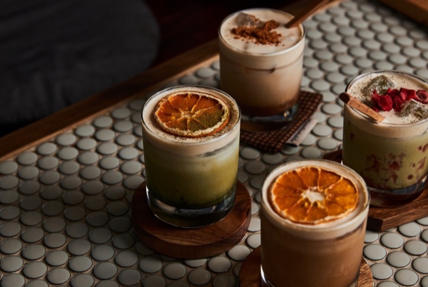 Four drinks garnished with dried fruit on a cafe tabletop.