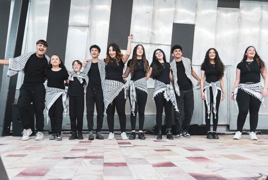 A group of young people all wearing black with black and white checked scarves tied around their waists.