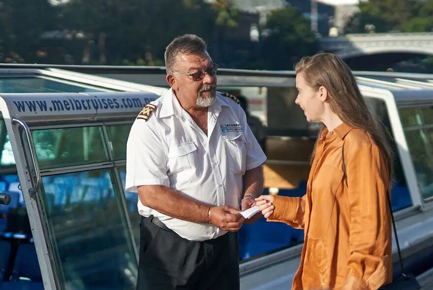 A captain of a ferry or boat service accepting a ticket from a person who is waiting to board the vessel.