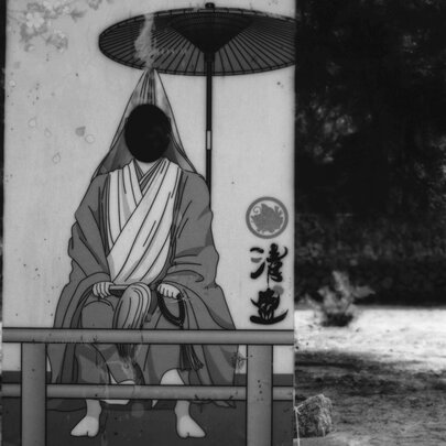 A saturated black and white images of a hooded figure sitting under a small parasol in Japan. 
