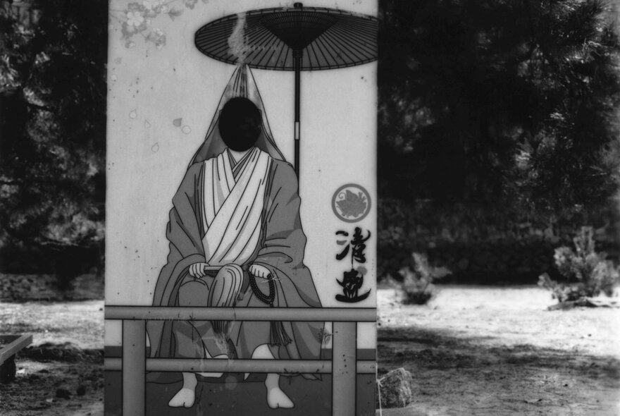 A saturated black and white images of a hooded figure sitting under a small parasol in Japan. 