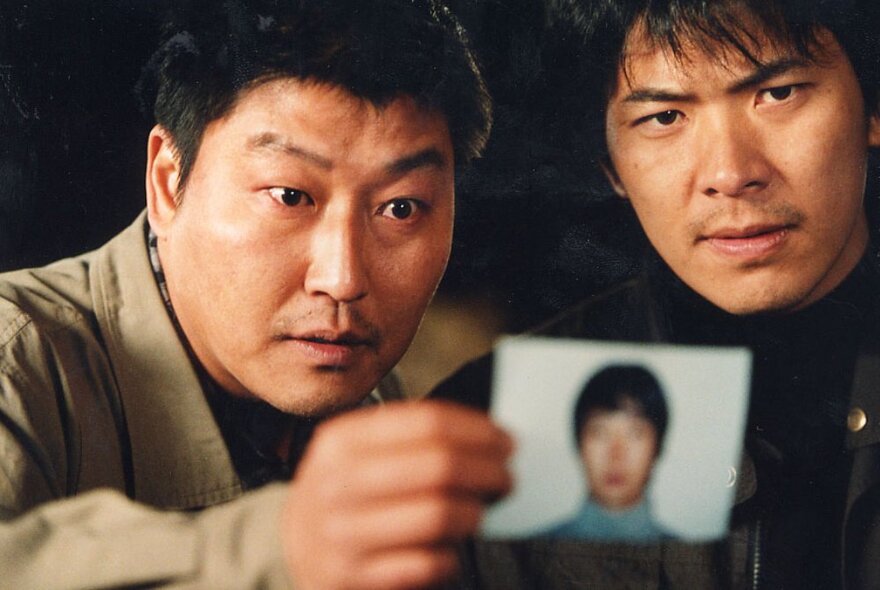 Two detectives hold forth a photo of a suspect in  a still image from the South Korean film Memories of Murder.