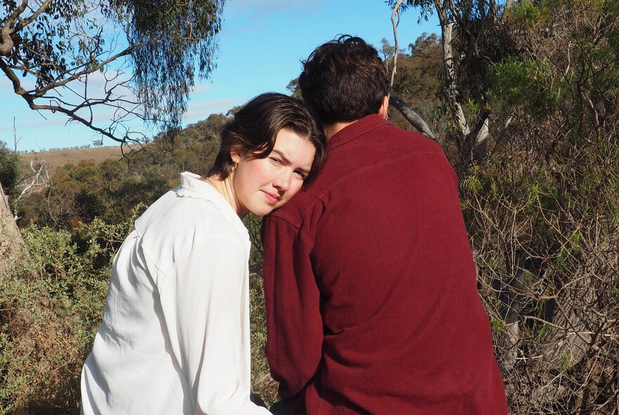 A woman leaning her head on a man's shoulder in a bush setting.