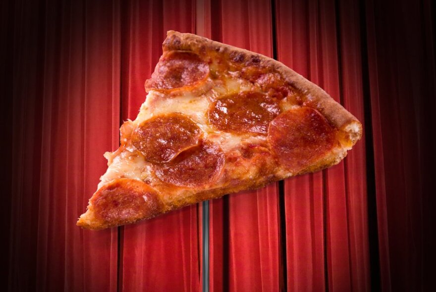 A slice of pepperoni pizza against a red curtain backdrop.