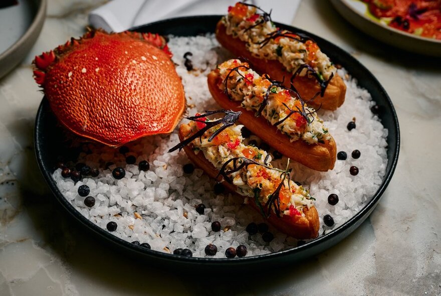 Crab on plate next to three finger shaped hors d'oeuvres.