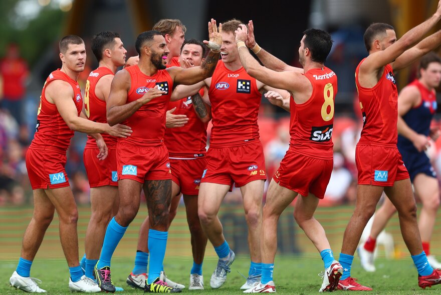 A large huddle of Gold Coast Suns AFL football players on the football field congratulating each other and high-fiving. 