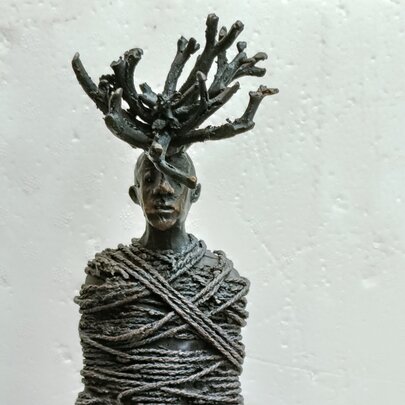 Bronze sculpture of a human figure with its torso tightly wrapped in thick ropes and a dense, antler-like crown of branches or roots  sprouting from the figure's head.