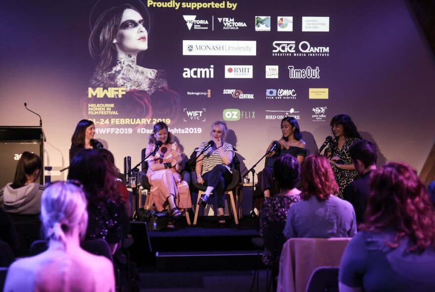 Panellists seated on stage in front of an audience and backscreen image.