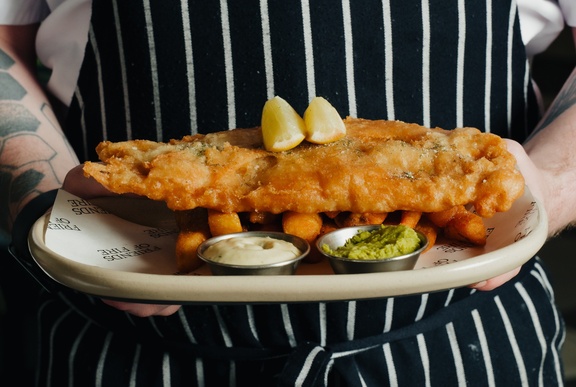 A chef holding a plate of gourmet fried fish on a bed of vegetables.