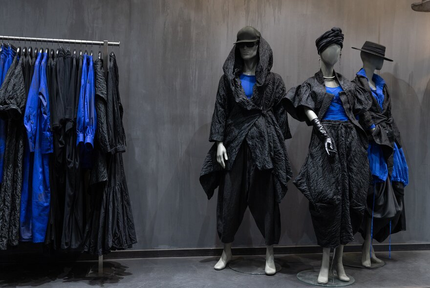 A rack of blue and black structural garments inside a shop, alongside three shop mannequins wearing the same black and cobalt blue garments.