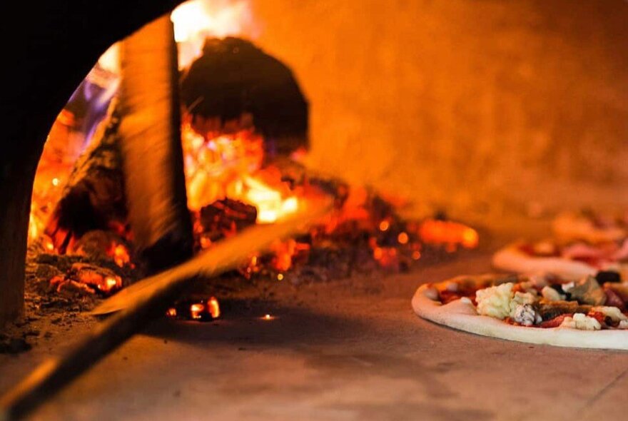 The fiery entrance to a wood-fired pizza oven, with a pizza waiting on the stone slab.
