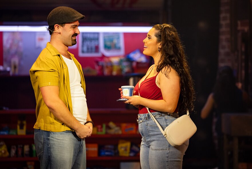Two actors talking and interacting on a theatre stage, one of them holding a cup of coffee.