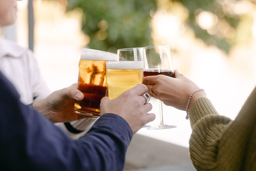 Hands clinking glasses of beer and wine at an outside bar.