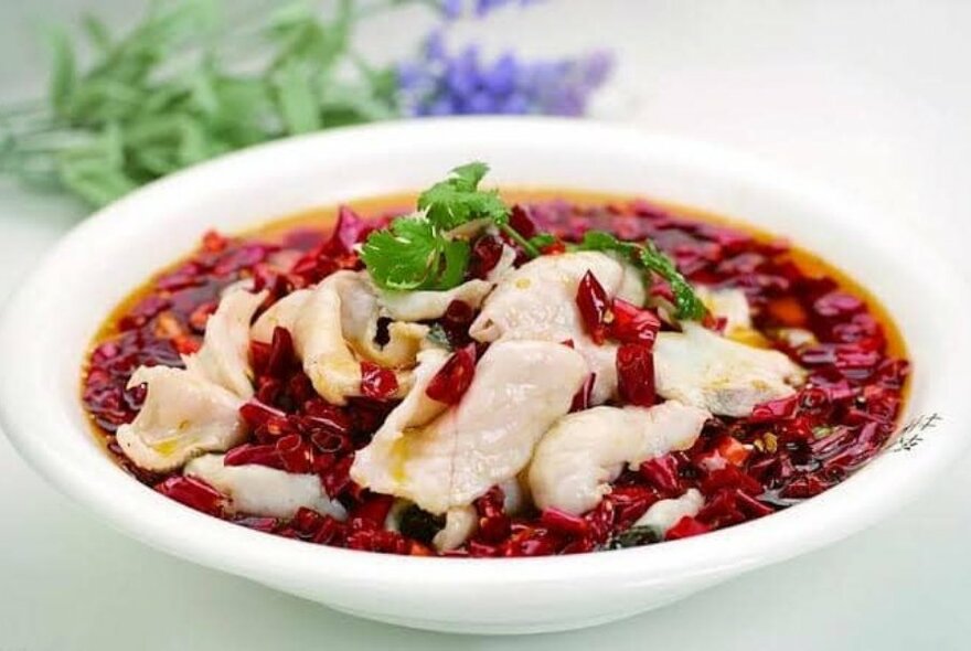 A bowl of chicken in chilli sauce with a sprig of lavender in the background. 