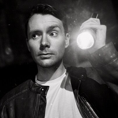 Comedian Matt Bell looking to the side with one eyebrow raised, holding a torch.