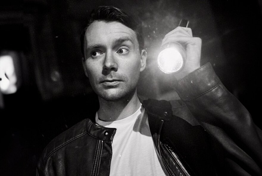 Comedian Matt Bell looking to the side with one eyebrow raised, holding a torch.