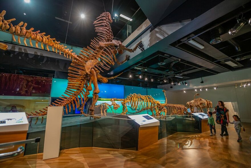 An adult and two children walking through a dinosaur museum exhibit.