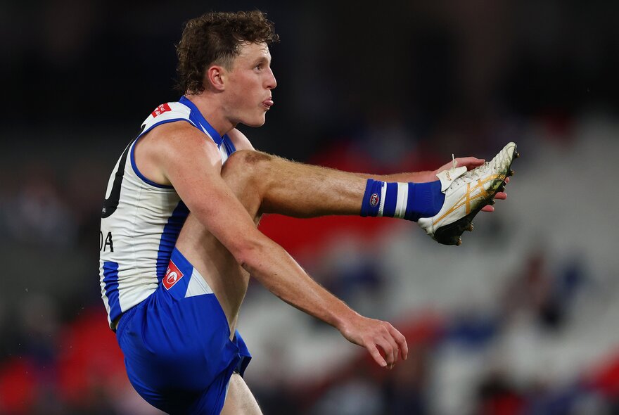 North Melbourne AFL football player with his leg raised in the air, having just kicked the ball, on the field during a match.