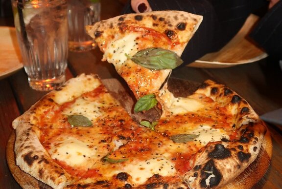 A wood-fired pizza with a slice being served.