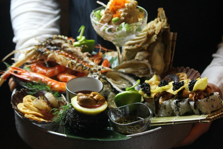 A waiter carrying a stacked seafood platter, filled with a variety of different dishes.