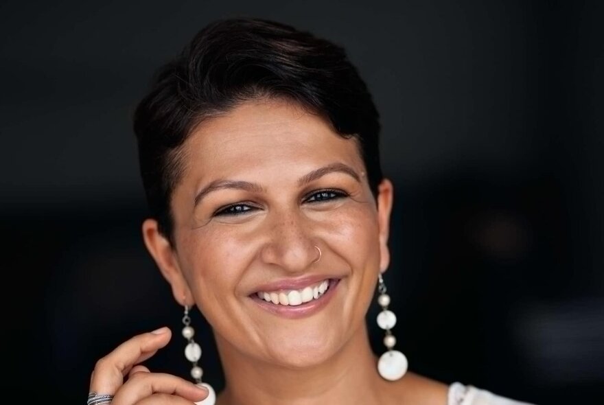 A woman with short black hair and long dangling earrings smiling warmly. 