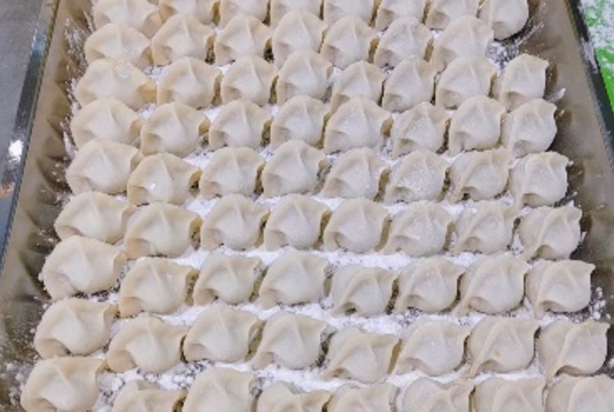 Rows of pleated dumplings on a tray.