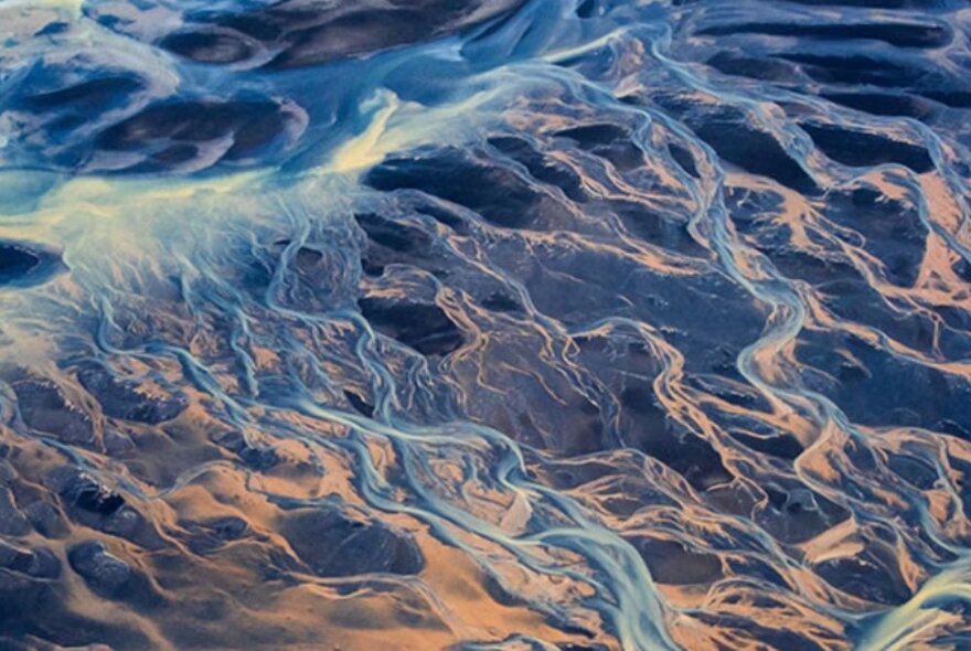 A pink and blue-toned depiction of a river and surrounding dunes, seen from above. 