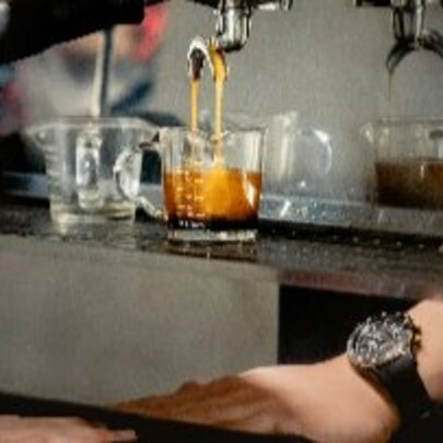 Barista's hand next to a coffee machine with liquid pouring into a glass.