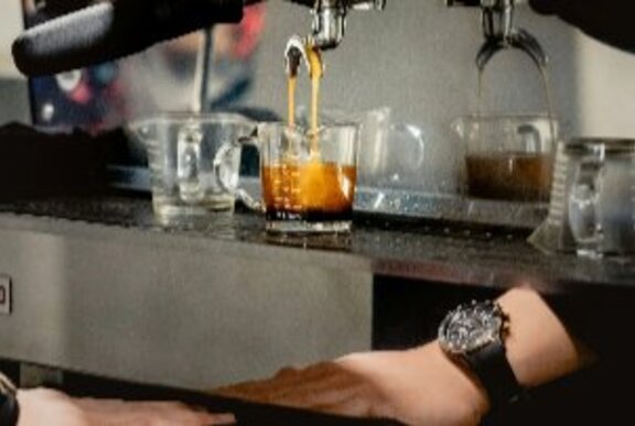 Barista's hand next to a coffee machine with liquid pouring into a glass.