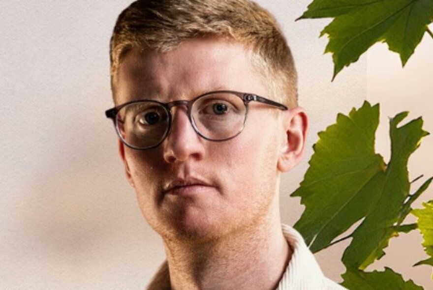 Serious-looking young man wearing spectacles posed next to a plant.