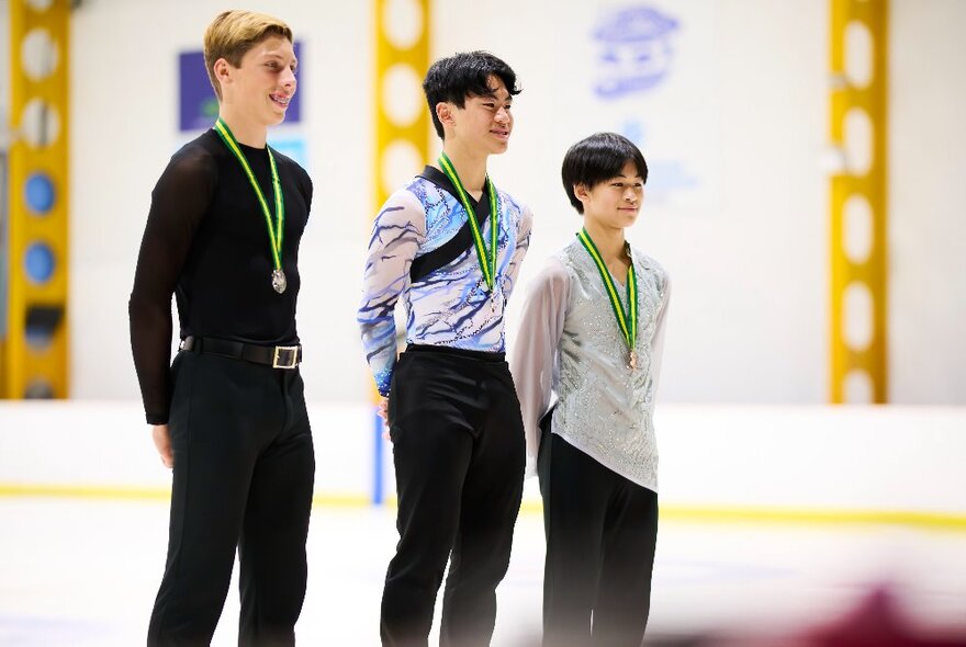 Three male figure skaters standing on a dais with medals around their necks.