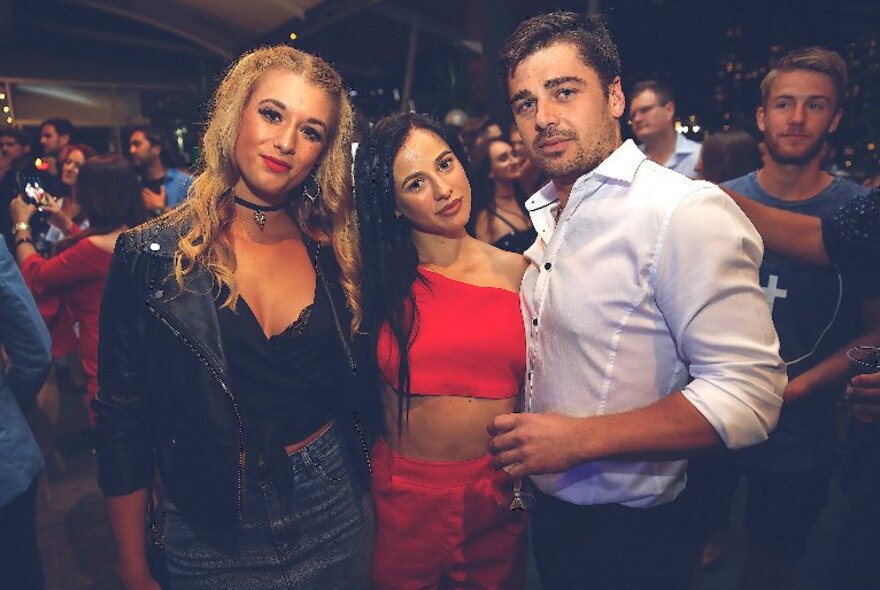 Three attractive people posing for a photo at a nightclub.