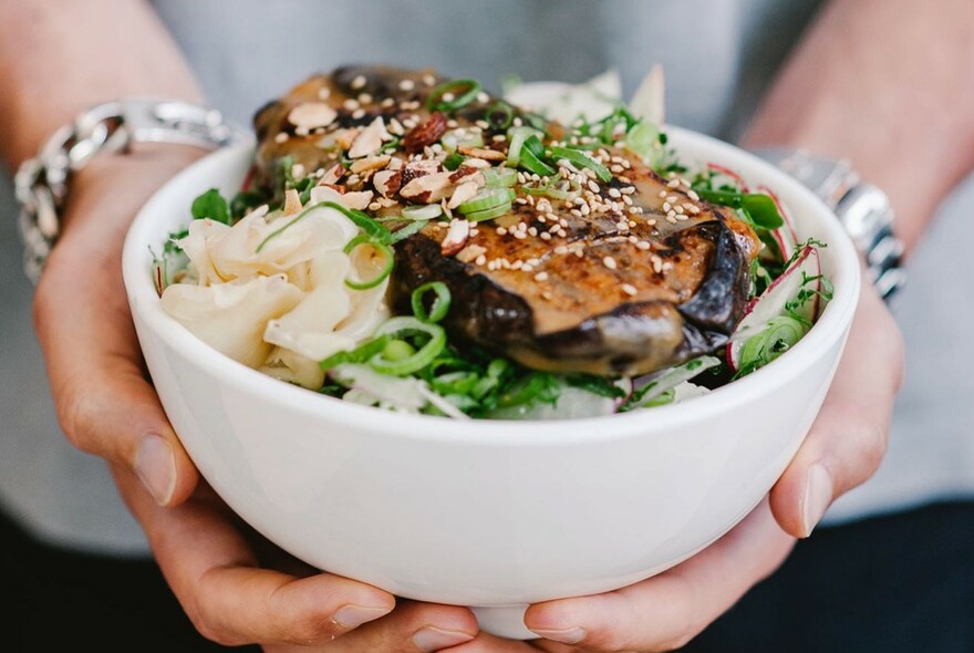 Two hands holding a brimming bowl of food.