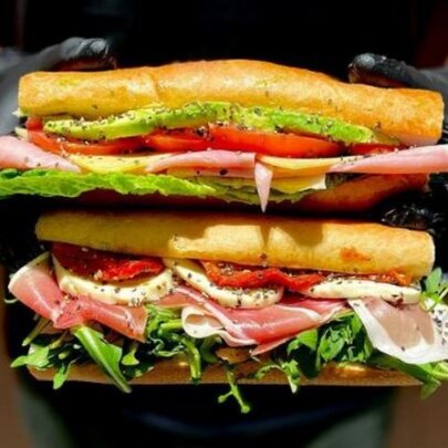 A pair of delicious looking filled french baguettes being held one above the other by two hands in black gloves.
