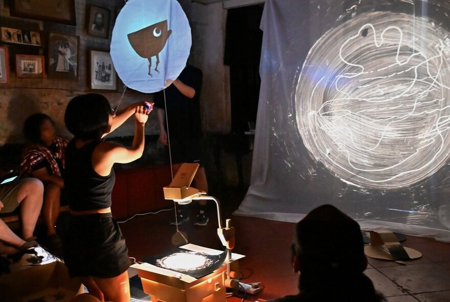 Puppeteer performing with a round puppet character in a darkened room.
